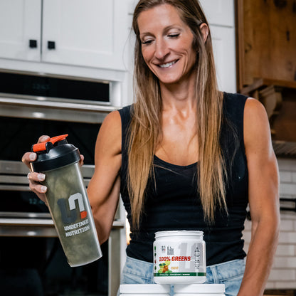 Keri Shaw holding a protein shaker and container in a kitchen setting